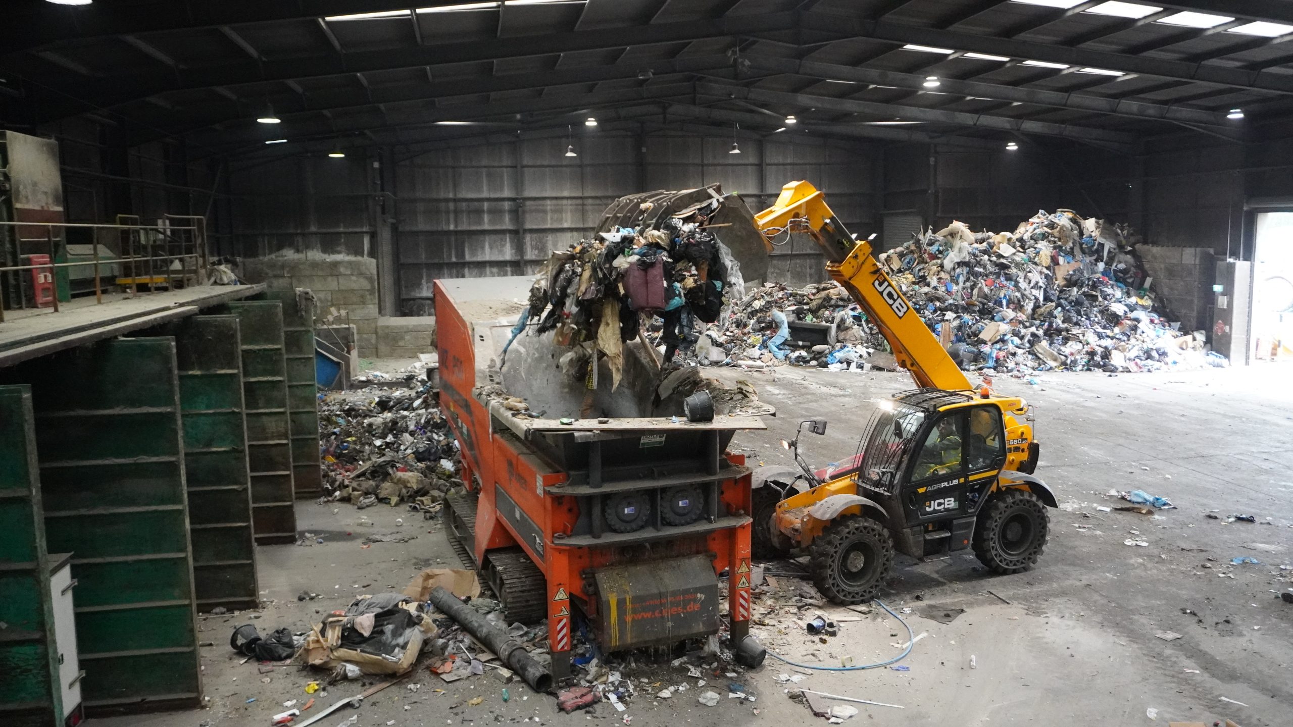 A JCB grabber dropping mixed waste into an industrial mulcher