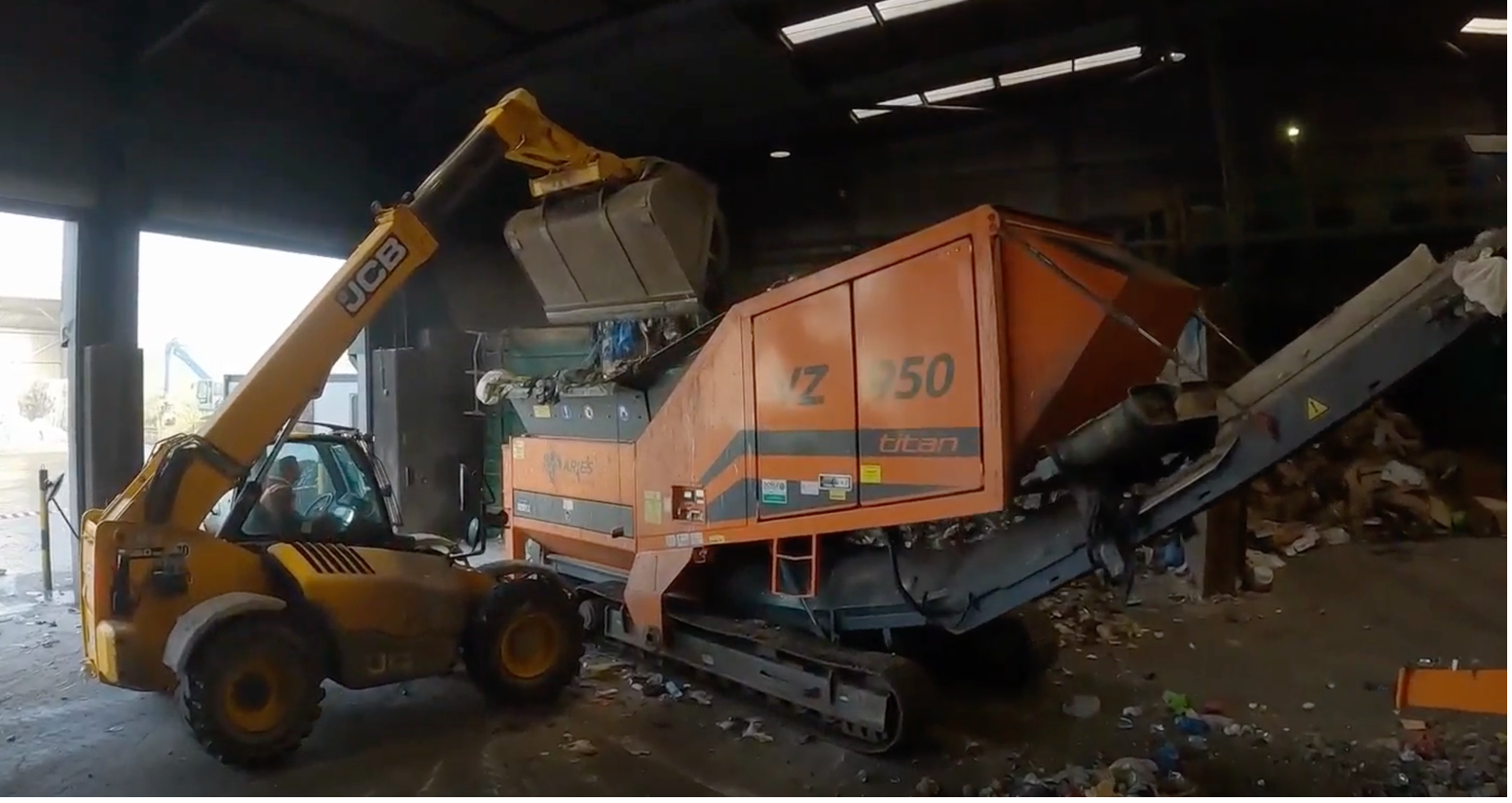 A yellow JCB grabber drops waste into an industrial mulcher