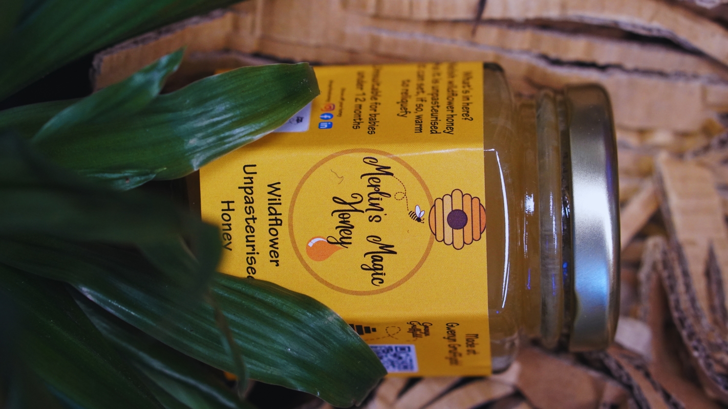 Jar of honey with yellow label with Merlin's Magic Honey in script font.