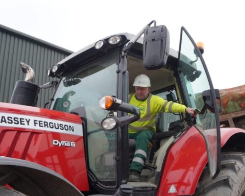 Worker in his-vis and a hard hat is getting out of a red tractor pulling a high sided trailer